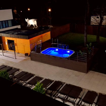 Panorama terenu zewnętrznego Strefy Saun nocą. Od lewej jacuzzi, prysznice zewnętrzne i duża sauna zewnętrzna, dalej rzędy leżaków i zewnętrzny basen z wodą zimną. Całość klimatycznie podświetlona.