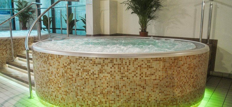 Wanna jacuzzi otoczona beżową mozaiką. Dolna krawędź wanny podświetlona na zielono.