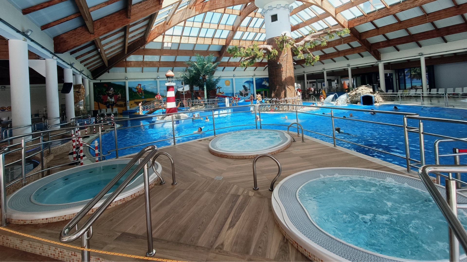 3 wanny jacuzzi w Strefie Basenowej. Wanny znajdują się na podeście z drewnopodobną podłogą. W tle widać basen rekreacyjny i pozostałe atrakcje w hali basenowej.