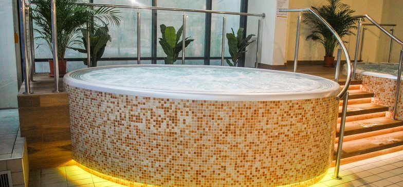Wanna jacuzzi otoczona beżową mozaiką. Dolne krawędzie wanny podświetlone na żółto.