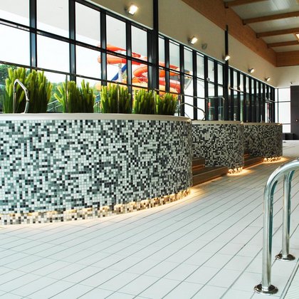 Trzy wanny jacuzzi obłożone szarą mozaiką ceramiczną ustawione wzdłuż przeszklonej ściany, za którą widać pomarańczową i czerwoną MegaZjeżdżalnie.