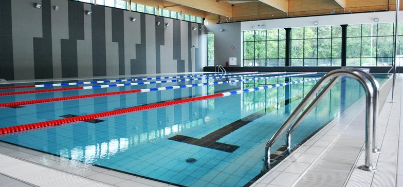 Wewnętrzny basen sportowy. Na pierwszym planie aluminiowa drabinka prowadząca do basenu.