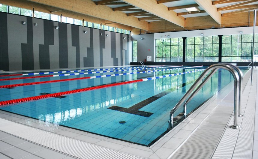 Wewnętrzny basen sportowy. Na pierwszym planie aluminiowa drabinka prowadząca do basenu.