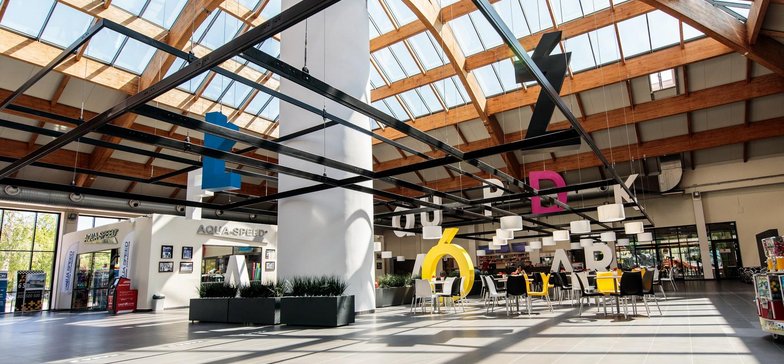 Restauracja w holu głównym Aquaparku. Na pierwszym planie kolorowe krzesełka i litery układające się w napis: Aquapark Łódź