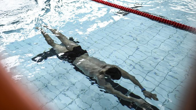 Mężczyzna w basenie sportowym, całkowicie zanurzony pod powierzchnią wody. 