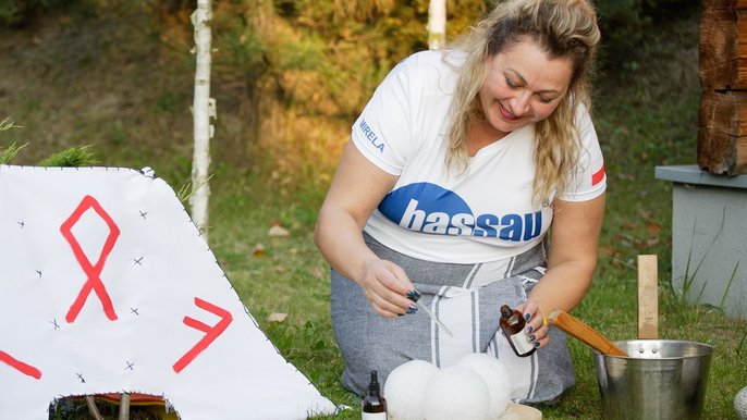 Saunamistrzyni Mirela Kazuś-Barańska - blondynka klęczy na ziemi i pochyla się nad trzema lodowymi kulami, które zakrapla olejkiem aromaterapeutycznym. 
