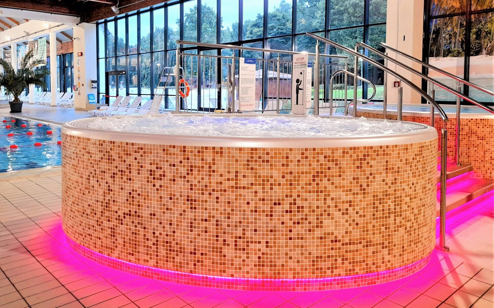 Wanna jacuzzi otoczona beżową mozaiką. Dolne krawędzie wanny podświetlone na różowo.