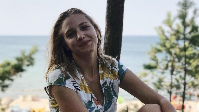 Saunamistrzyni Monika Klag - młoda blondynka w jasnej sukience w kwiaty pozuje z uśmiechem na tle terenów leśnych nad brzegiem morza. 