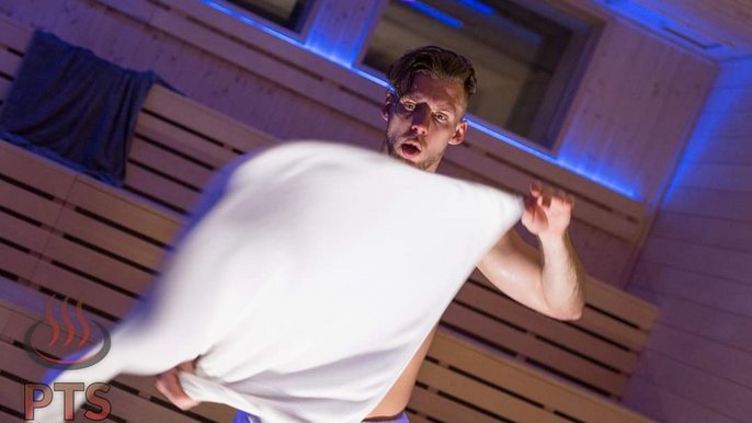 Saunamistrz Kacper Danisiewicz. Młody blondyn z niewielkim zarostem wewnątrz sauny trzyma przed sobą szeroko rozłożony biały ręcznik. Fot. Ryszard Rak. 