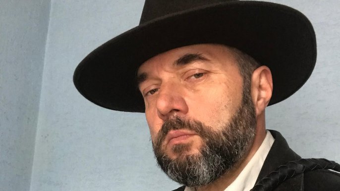 Saunamistrz Wojciech Draga. Zbliżenie na mężczyznę w ciemnym kapeluszu i z brodą, który spogląda z powagą w obiektyw. 