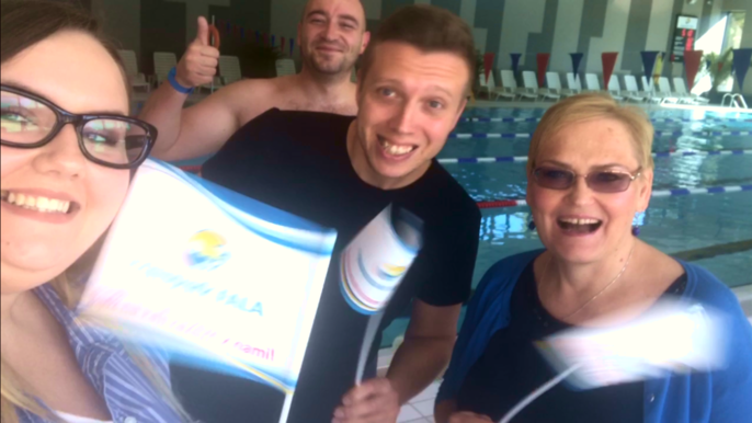 Pracownicy Aquaparku z uśmiechem pozują na tle basenu sportowego. Od lewej kobieta w okularach, po środku uśmiechnięty mężczyzna w czarnej koszulce, a po prawo blondynka w ciemnych okularach. Za nimi do zdjęcia włączył się Falowicz. 