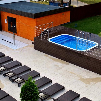 Panorama terenu zewnętrznego Strefy Saun. Od lewej jacuzzi, trzy poczwórne prysznice zewnętrzne, duża sauna zewnętrzna, basen wody zimnej i rzędy brązowych leżaków.