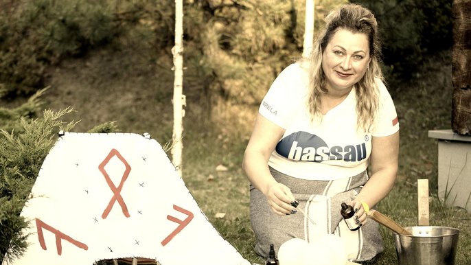 Zdjęcie w kolorach sepii. Saunamistrzyni Mirela Kazuś Barańska klęczy w leśnej scenerii zakraplając trzy lodowe kule olejkami eterycznymi. Po lewej leży biały wachlarz saunowy. 