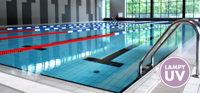 Wewnętrzny basen sportowy z wyznaczonymi torami pływackimi. Na pierwszym planie drabinka aluminiowa. W prawym dolnym rogu znak informacyjny: LAMPY UV.