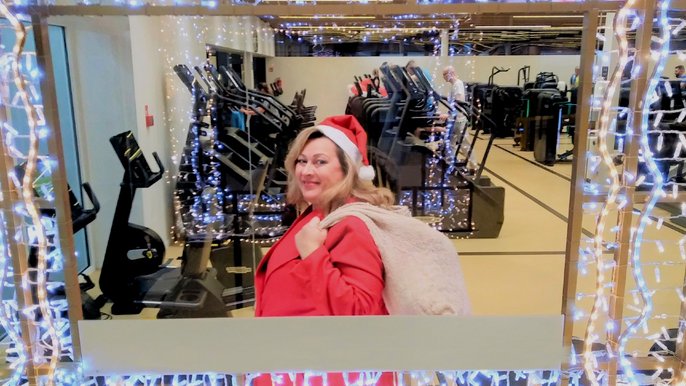 Sanamistrzyni Mirella Kazuś-Barańska. Ubrana jest w czerwony strój mikołaja i ma zarzucony na plecy worek z prezentami. Otacza ją ramka ze światełek choinkowych. Pozuje na tle siłowni udekorowanej na Święta. 