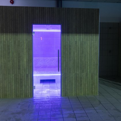 Sauna parowa od zewnątrz obita ceramiką imitującą cienkie, drewniane deski. Wnętrze sauny podświetlone w kolorze fioletowym.