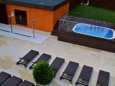 Panorama terenu zewnętrznego Strefy Saun. Od lewej duża sauna zewnętrzna, dalej basen wody zimnej i kawałek zielonego trawnika, a poniżej plaża z rzędami ciemnych ręczników.