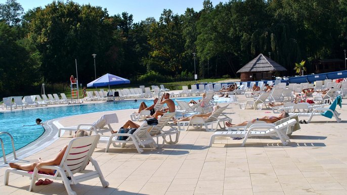 Plaża wokół basenu wypływowego w słoneczny dzień. Na białych leżakach relaksuje się sporo Falowiczów korzystając z pięknej pogody. 